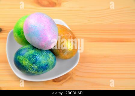 Colored eggs in a white plate on a natural wooden fuzzy background Stock Photo