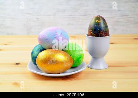 Colored eggs in a white plate on a natural wooden fuzzy background Stock Photo