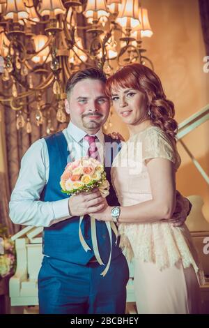 Bridal couple in front of a piano . Happy wedding day. Happy bride and groom near piano in white interior studio . Newlyweds stand in the interior Stock Photo