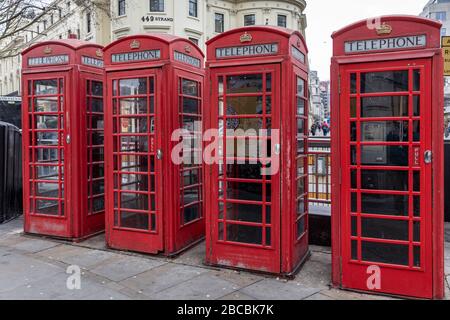Four red traditional and heritage telephone boxes stand in a row on the Strand, London, England, UK opposite Charing Cross Station. Stock Photo