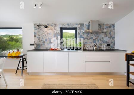 White modern kitchen with abstract backsplash and wooden floor. Stock Photo