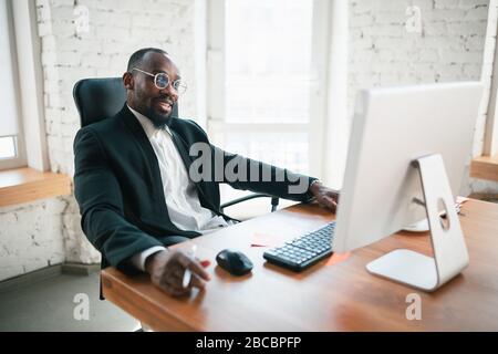 Calling, talking on phone. African-american entrepreneur, businessman working concentrated in office. Looks serios, busy, wearing classic suit. Concept of work, finance, business, success, leadership. Stock Photo