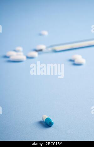 Pills, tablets and analog thermometer on bright blue background, healthcare medical concept, antibiotics and cure, angle view selective photo Stock Photo