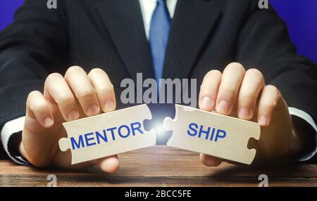Businessman collects wooden puzzles with the words Mentorship. Business support. The concept of personal and professional development and training by Stock Photo