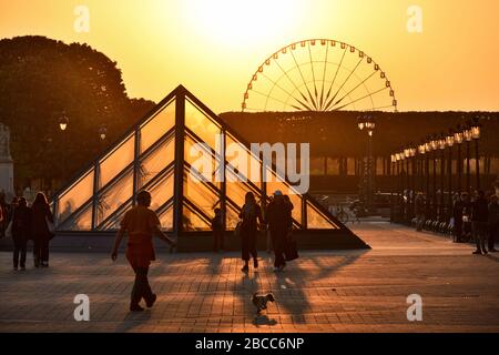 PARIS, FRANCE - MAY 4, 2018: The Louvre museum and a big wheel in the background illuminated by the sunset. Stock Photo