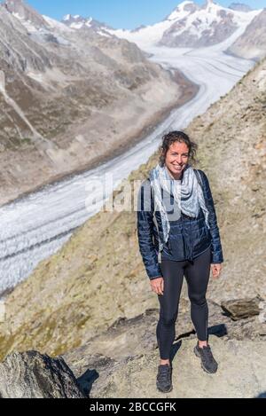 Young Caucasian woman posing for the camera, with the Great Aletsch Glacier behind her