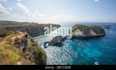 Bali, Indonesia-3 Aug 2019: A tourist looks down at the cliff rock formation in Atuh Beach bay, in Nusa Penida Island, near Bali, Indonesia Stock Photo