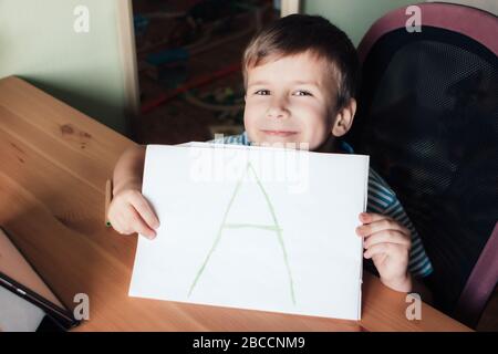 Happy satisfied boy shows page with handwritten letter A, home education concept Stock Photo