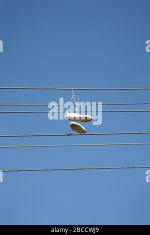 a pair of trainers thrown over a power line, commonly believed  to signal the location of a crack house / drug dealing spot. Can also be the symbol of Stock Photo