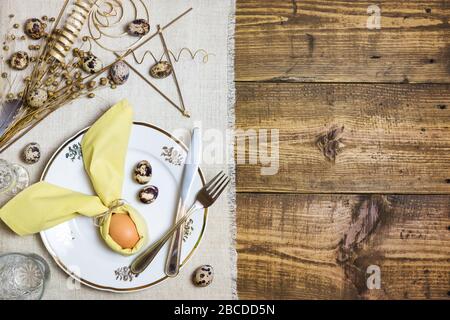 Festive Easter table setting with egg in napkin like Easter Bunny and quail eggs on rustic background. Top view with copy space. Stock Photo