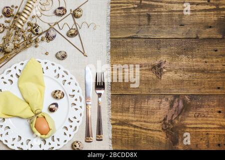 Festive Easter table setting with egg in napkin like Easter Bunny and quail eggs on rustic background. Top view with copy space. Stock Photo