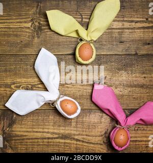 Beautiful Easter background with eggs in napkins like Easter Bunny on rustic wooden table. Top view with space for text. Stock Photo