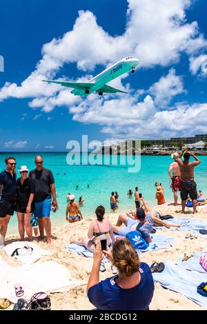 Woman taking photo of a family on Maho Beach as a McDonnell Douglas MD83 airplane of Inselair flies overhead Stock Photo