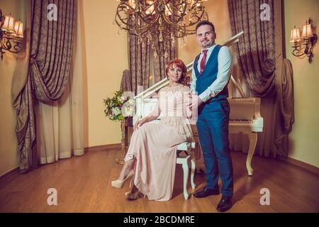 Bridal couple in front of a piano . Happy wedding day. Happy bride and groom near piano in white interior studio . Newlyweds stand in the interior Stock Photo