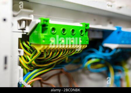 Green-yellow self-locking block for the grounding electric wire, mounted in the electric box with connected cables. Stock Photo
