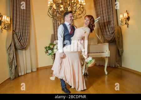 Bridal couple in front of a piano . Happy wedding day. Happy bride and groom near piano in white interior studio . Newlyweds stand in the interior Stock Photo