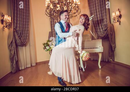 Bridal couple in front of a piano . Happy wedding day. Happy bride and groom near piano in white interior studio . Newlyweds stand in the interior Stock Photo