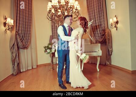 Bridal couple in front of a piano . Happy wedding day. Happy bride and groom near piano in white interior studio . Newlyweds stand in the interior Stock Photo