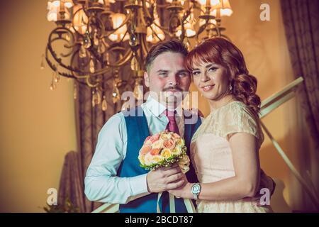 Bridal couple in front of a piano . Happy wedding day. Happy bride and groom near piano in white interior studio . Newlyweds stand in the interior Stock Photo