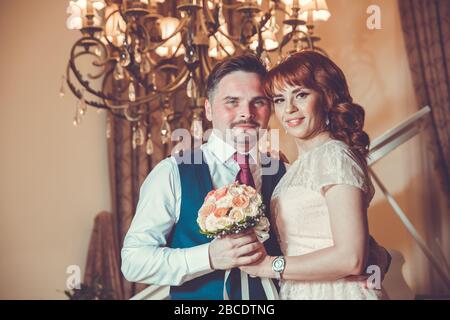 Bridal couple in front of a piano . Happy wedding day. Happy bride and groom near piano in white interior studio . Newlyweds stand in the interior Stock Photo