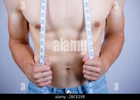 Always in good shape. Cropped image of muscular man measuring his waist  with measuring tape Stock Photo by gstockstudio