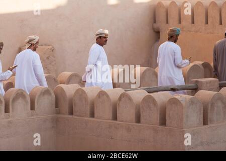 Omani men wearing dish dash's wander around the ancient ramparts of Nizwa Fort, Nizwa, Oman Stock Photo