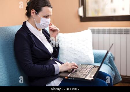 Woman with medical mask working on laptop, at home, concept of home working during quarantine Stock Photo
