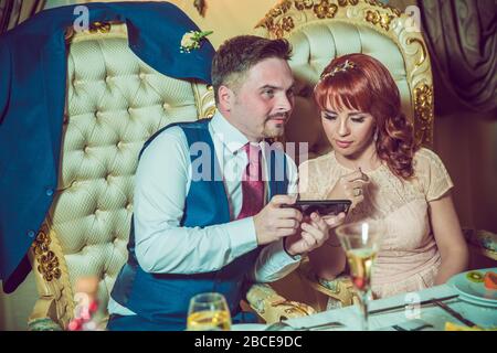 A bride and groom using a mobile phone . Close-up of beautiful bride sitting in a restaurant , taking a photo on the phone. phone during wedding Stock Photo