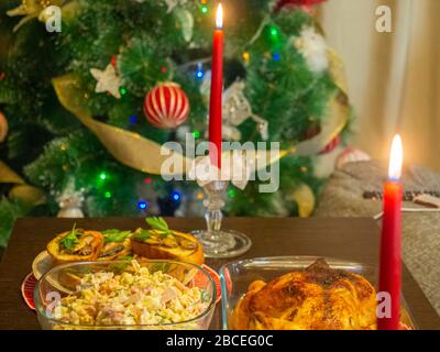 Fragment of a table with a Christmas dinner with burning candles on a background of the Christmas tree Stock Photo