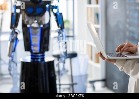 Hand of teenage student or programmer developing new software or working over technical project with robot on background Stock Photo