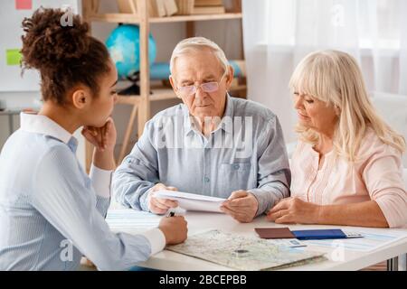Travel agent at office sitting with senior clients man looking at agreement thoughtful Stock Photo