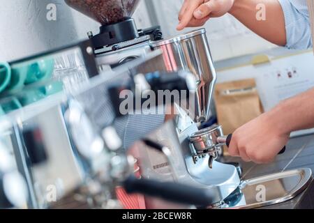 Coffee Passion. Young barista at coffee shop using electric coffee grinder making perfect grounds close-up Stock Photo