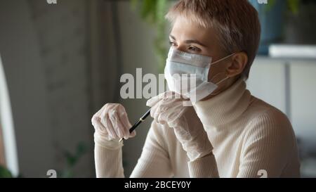 Pensive young businesswoman in medical gloves and protective facial mask. Stock Photo