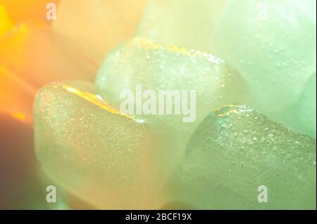 Green ice cube close up view on blurred colorful background Stock Photo