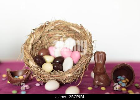 Bird nest with easter almonds, chocolate eggs with sweets and chocolate bunny on pink table Stock Photo