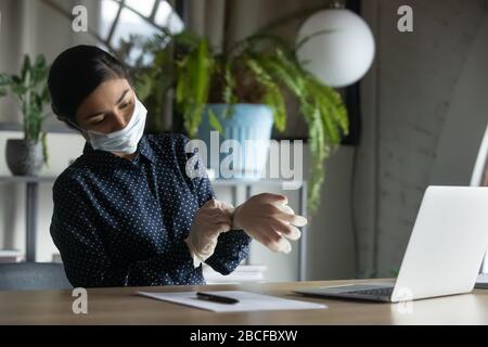 Young female company employee putting on medical gloves, starting workday. Stock Photo