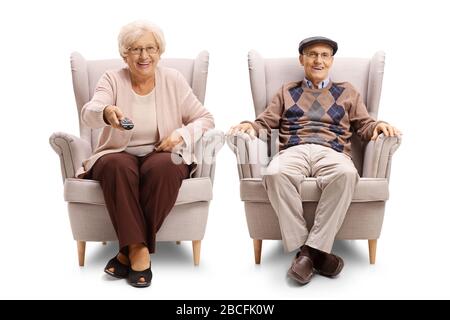 Senior couple sitting in an armchairs and holding a tv remote control isolated on white background Stock Photo