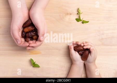 Ramadan concept. Kids holding dried date on old wooden table, Flat lay and top view Stock Photo
