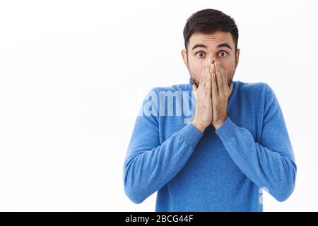 Close-up portrait of shocked, startled young man shut mouth with hands and express awe, amazement with eyes, gazing camera astounded, found out Stock Photo