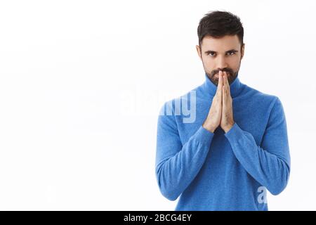 Portrait of hopeful handsome smart man, scheming something, have interesting idea, hold hands in pray, awaiting for relish, look confident at camera Stock Photo