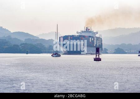 Container vessel meets a sailing yacht in the Gatun lake, section of Panama Canal Stock Photo