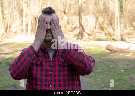 Man with hands on face. Person in meditative state doing yoga in nature. Young man with piercing with both hands on head standing in nature. Weird spi Stock Photo