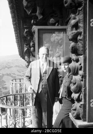 American businessman, newspaper publisher, and politician William Randolph Hearst (1863 - 1951) stands with Margaret Holmes (née Margaret Elisa Oliver, 1879-1968), wife of traveler, photographer and filmmaker Elias Burton Holmes, on the balcony of Hearst's Castle, San Simeon, California, 1931. Photography by Burton Holmes. Stock Photo