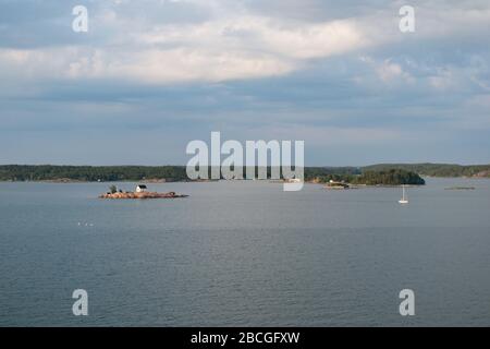 Panoramic view of a tiny cottage on a small, rocky island in the Turku archipelago with a sailing boat passing through the bay. Stock Photo