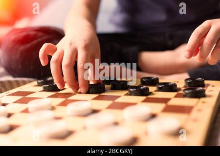 tay at home Quarantine concept. Young kid hands playing checkers table game on bed. Board game and kids leisure concept. Family time.  Stock Photo