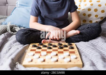 Young kid hands playing checkers table game on bed. Stay at home Quarantine concept. Board game and kids leisure concept. Family time.  Stock Photo
