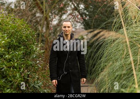 Smiling Caucasian Young Man with Earphones in Garden Stock Photo