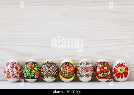 Colorful Easter eggs with ornament on light wooden boards background. Holiday greeting card, paschal mockup, frame with place for text, copy space Stock Photo