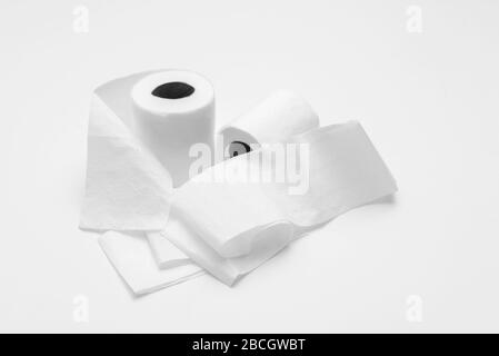 Two rolls of white toilet paper on white background, partly unrolled, viewed from an angle