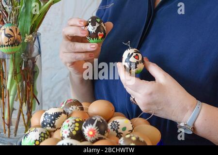 Female hands holding colorfully decorated Easter eggs with paper cuttings. Natural and patterned eggs placed on the front. A vase with a bouquet Stock Photo
